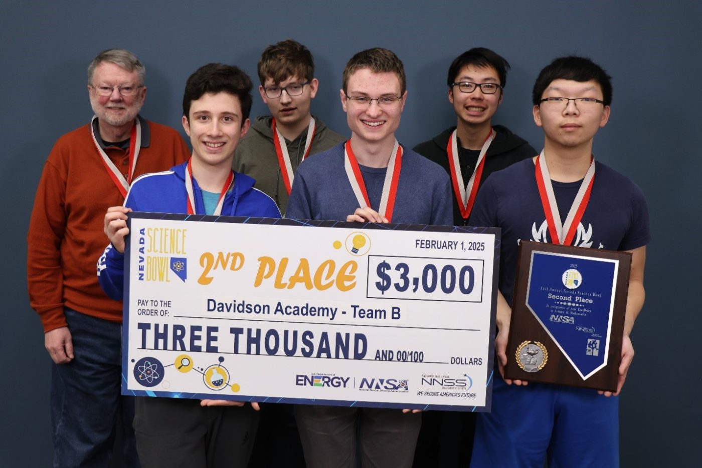 Students and their coach hold an oversized check marked $3,000.