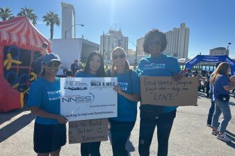 Four NNSS employees hold signs in support of the Walk a Mile in My Shoes campaign.