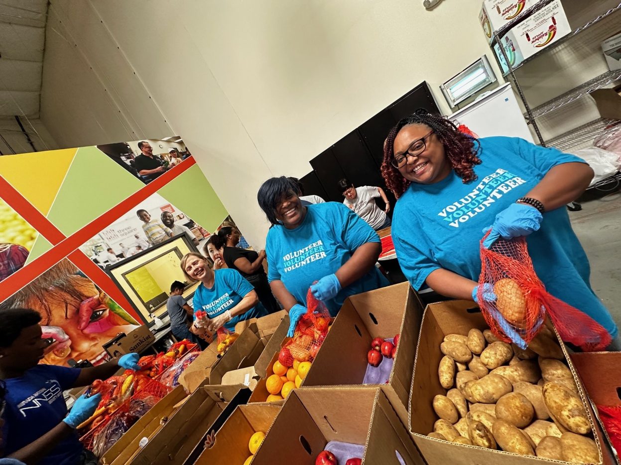 Volunteers in blue shirts pack vegetables and fruit into meal bags. 