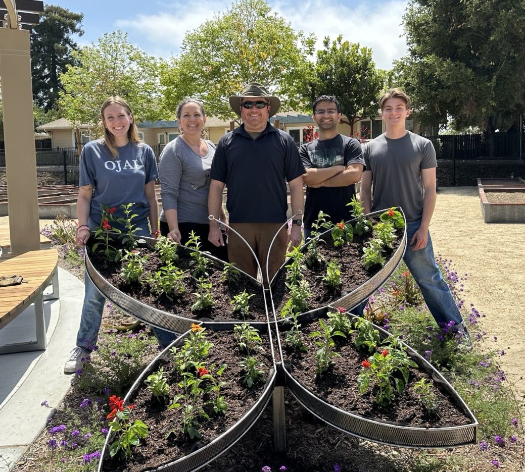 Five employees in gardening gear stand behind a planter in the shape of a butterfly. 