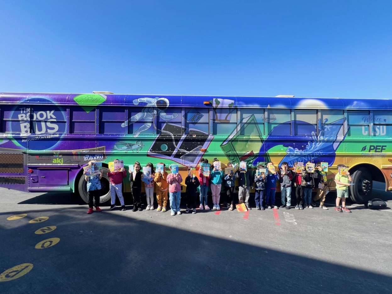 Students line up in front of a colorful bus while displaying books they selected for reading.