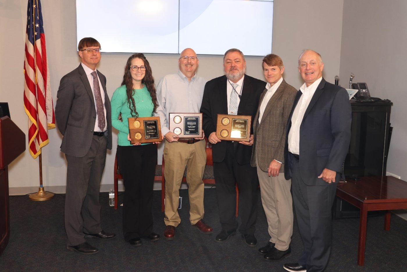 Six people representing the NNSS and NNSA stand with three award plaques.