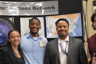 Three interns and a NNSS leader smile in front of Emergency Communications Network signage.