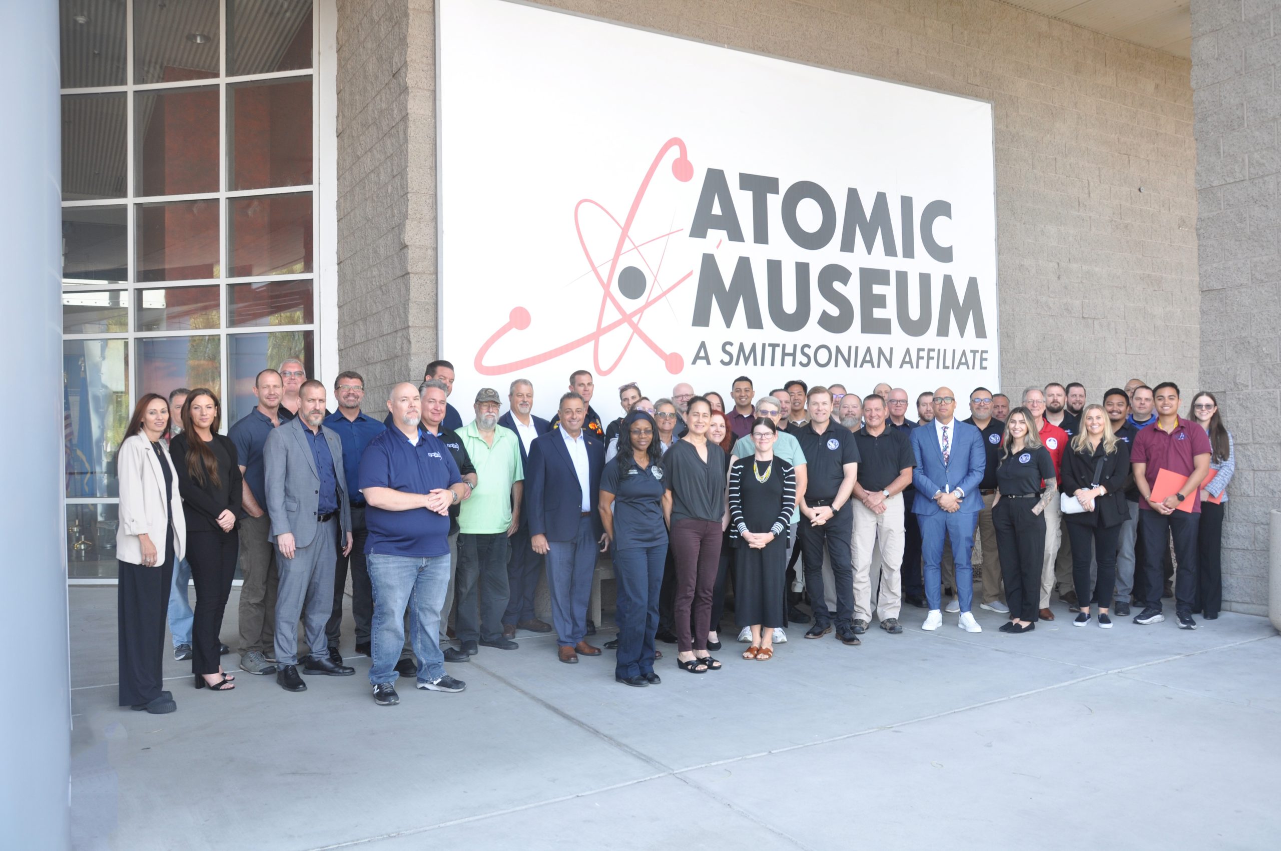 A group of emergency management leaders stands beneath the Atomic Museum's welcome sign.