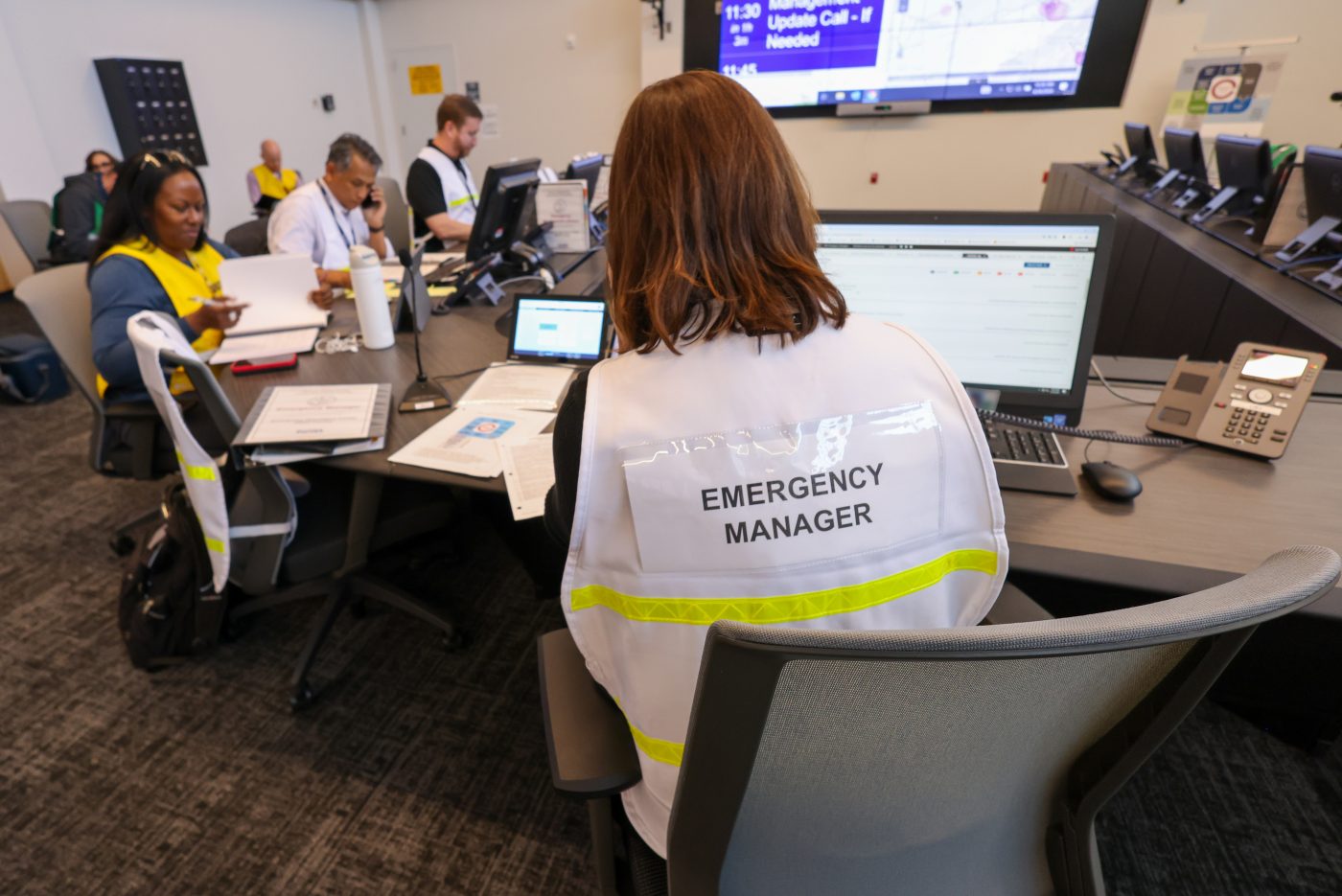 An emergency manager sits at a table with command staff members. 