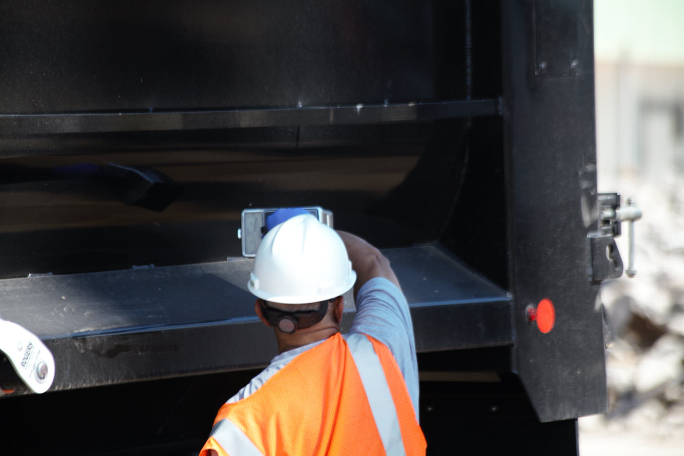 man in hard hat and orange vest scanning the back of a truck