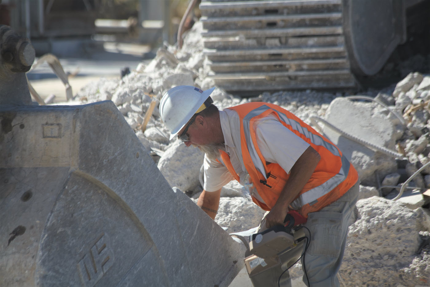 man in hard hat and orange vest scanning an excavator bucket with rubble in background