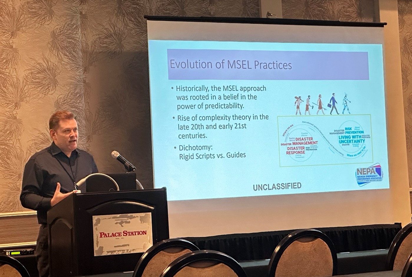 A NNSS Security and Emergency Services leader speaks at a podium in front of a presentation slide titled, "Evolution of MSEL Practices."