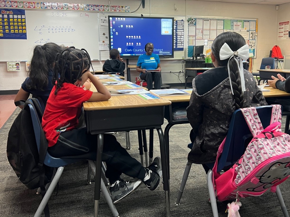 A NNSS volunteer smiles in front of a classroom of first grade students.