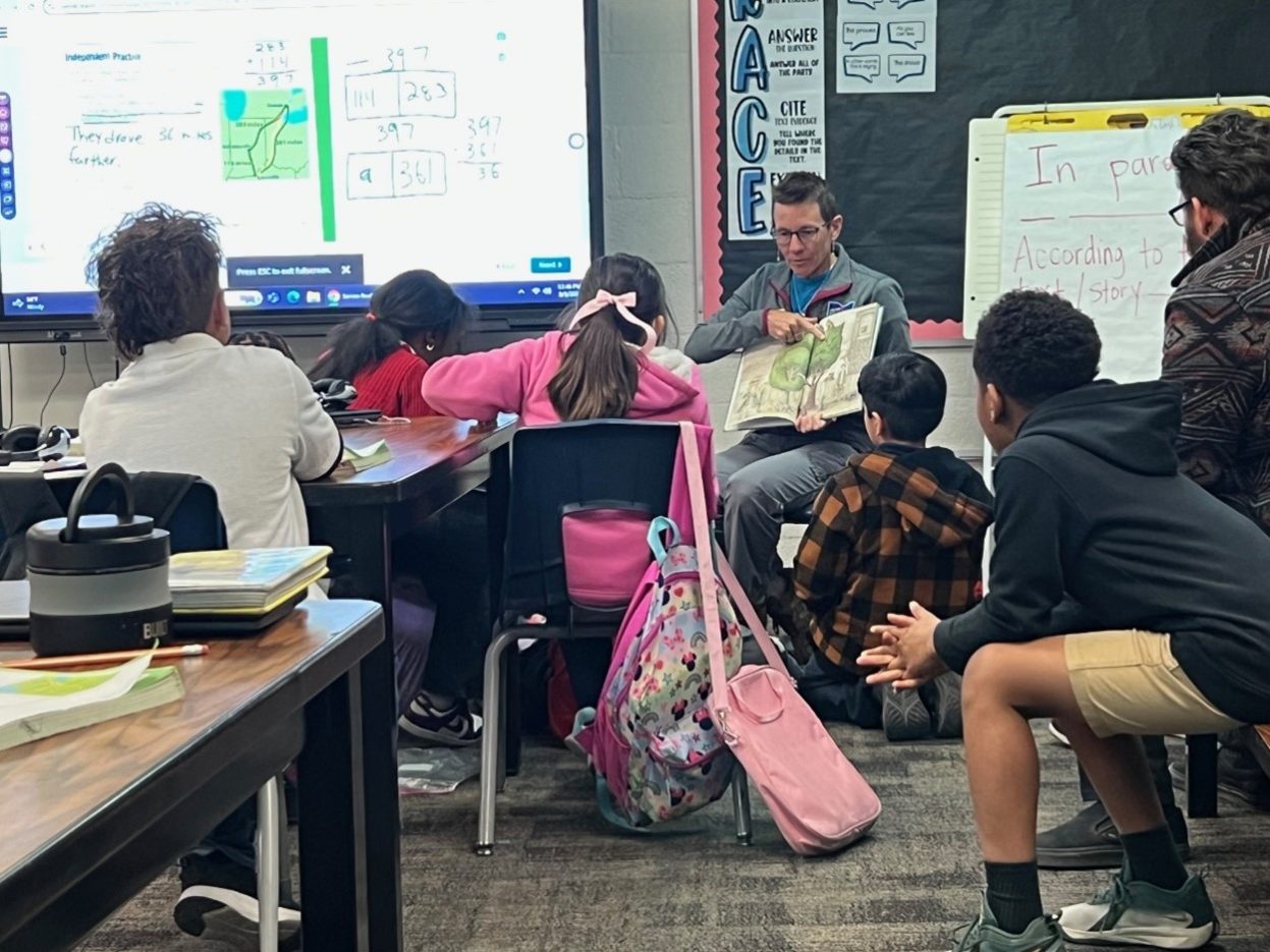 A NNSS volunteer reads to a classroom of third grade students.