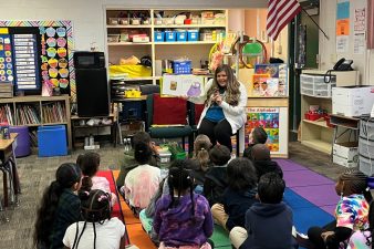 A NNSS volunteer shows book illustrations to a classroom of elementary students.