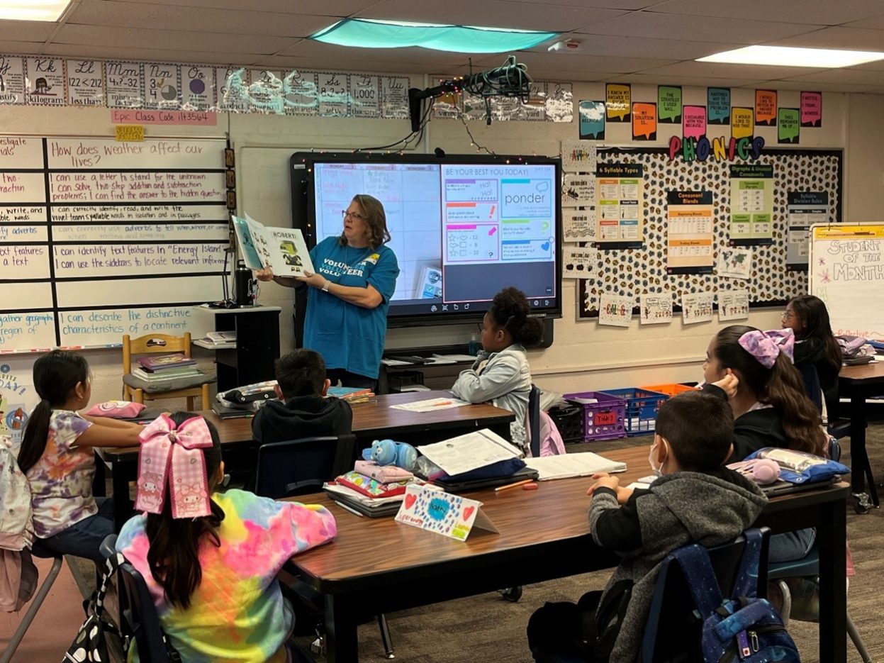 A NNSS volunteer shows book illustrations to a classroom of elementary students.