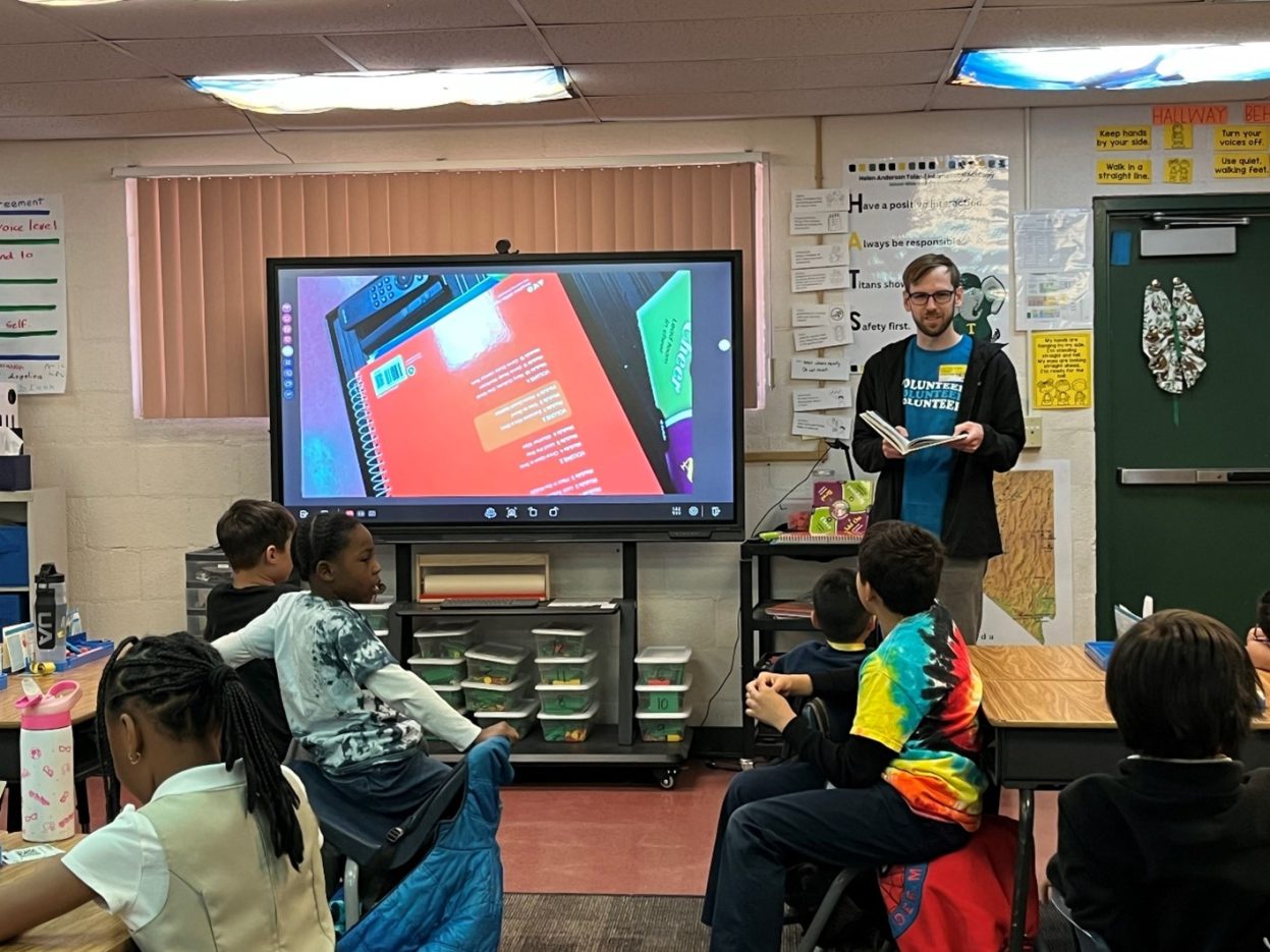 A NNSS volunteer shows reads to a classroom of elementary students.