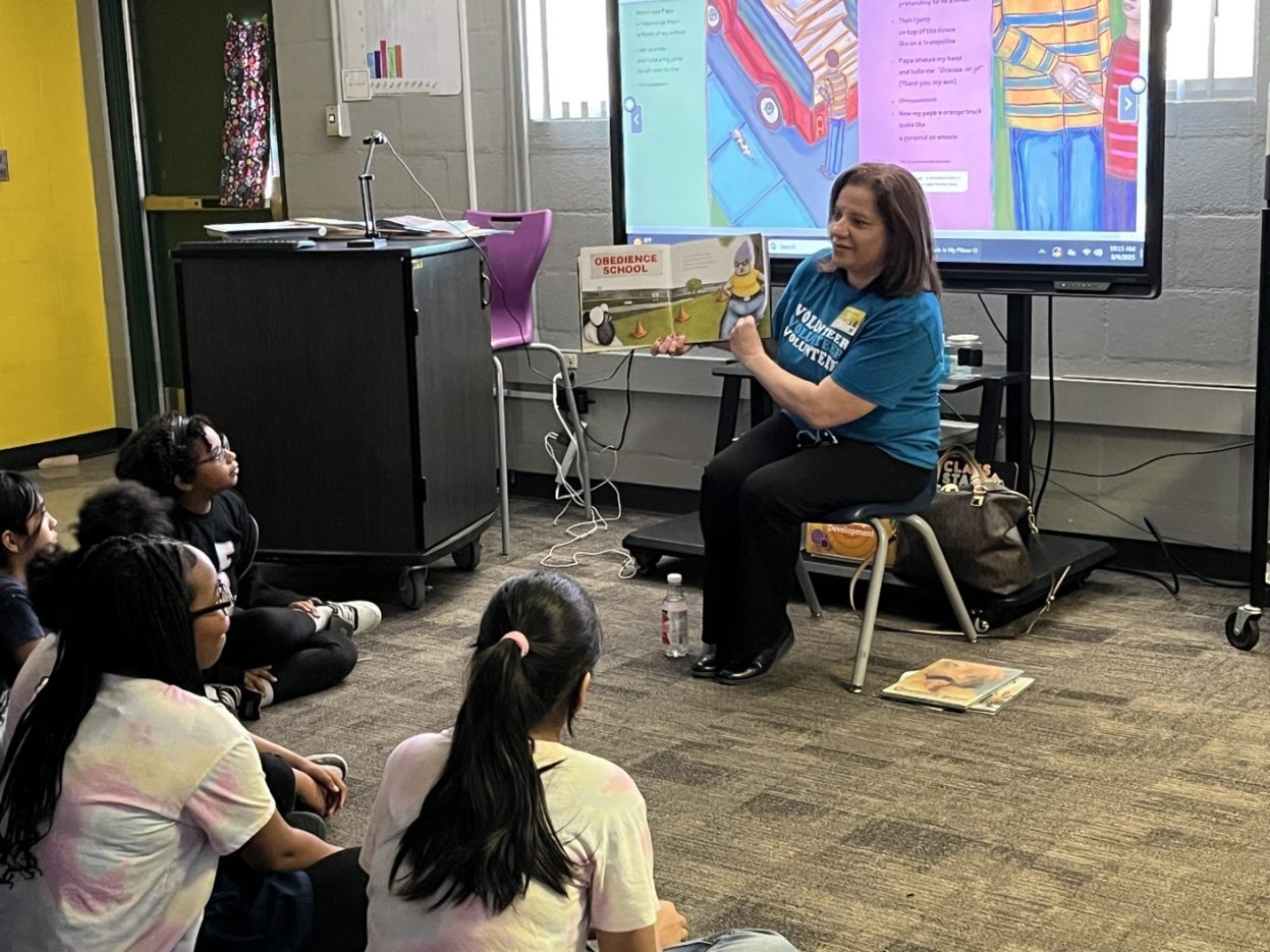 A NNSS volunteer shows book illustrations to a classroom of elementary students.