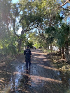 A hazmat response team member walks through a neighborhood with fallen trees, 