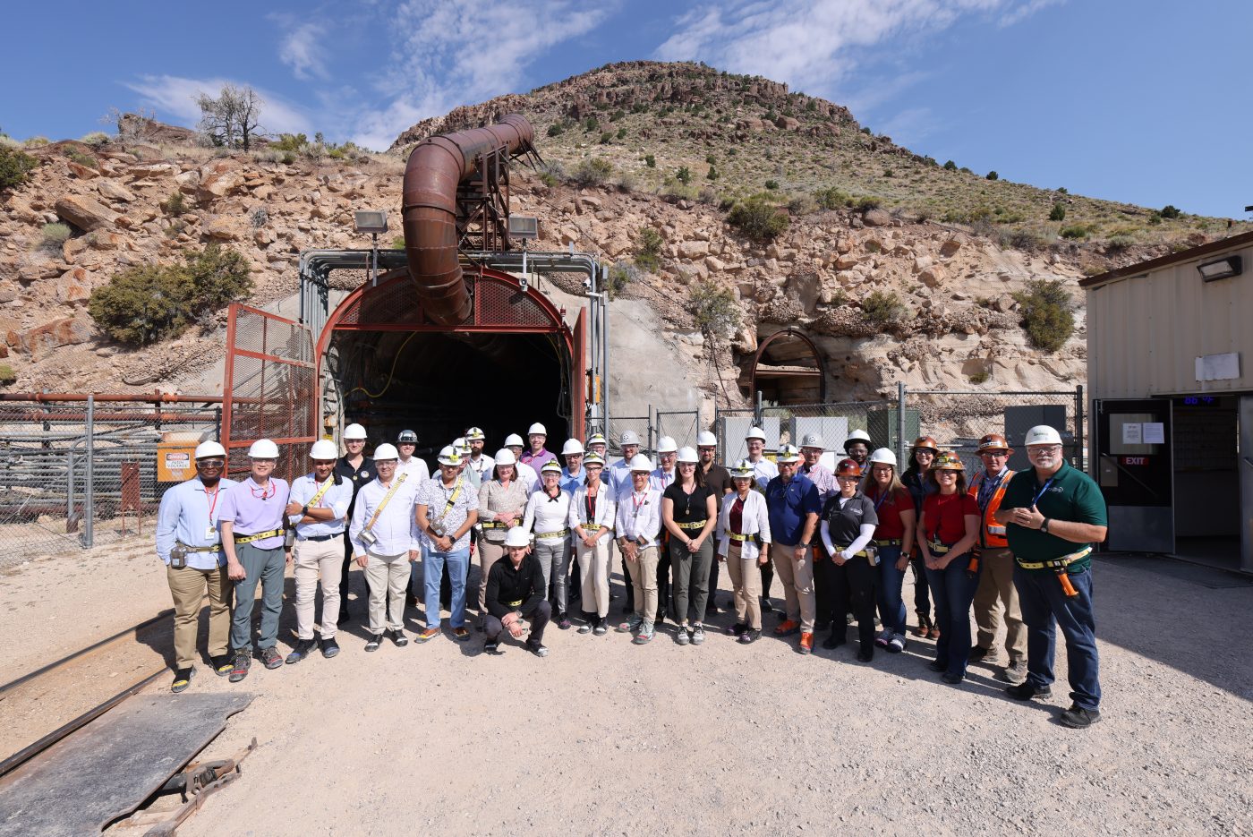 large group of people in hard hats stand in front of tunnel entrance