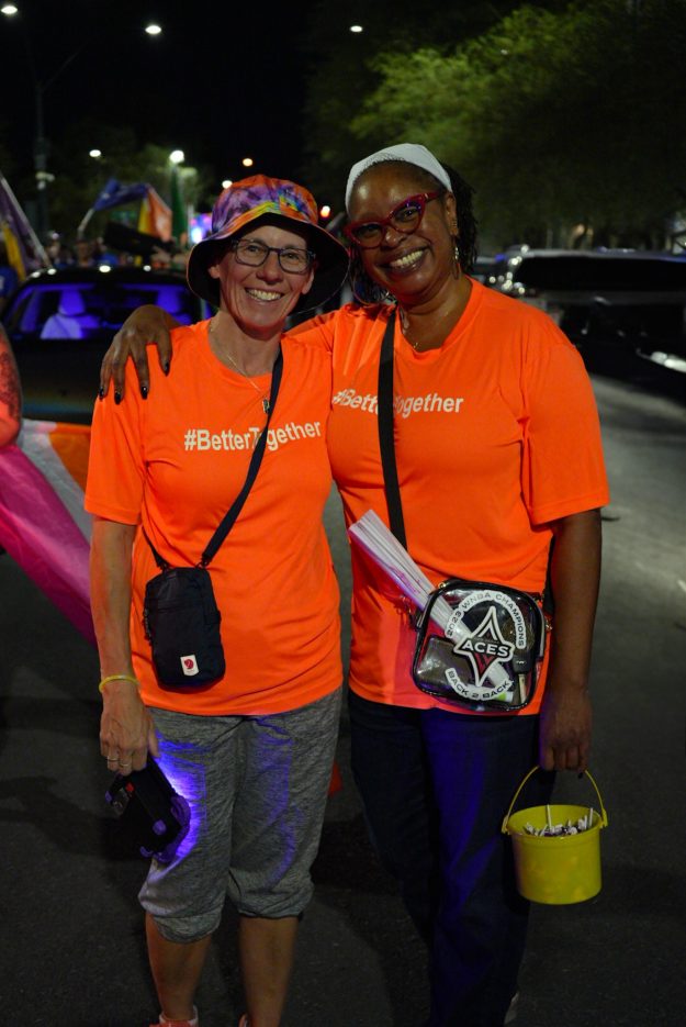 Two employees wearing orange shirts smile at Las Vegas PRIDE.