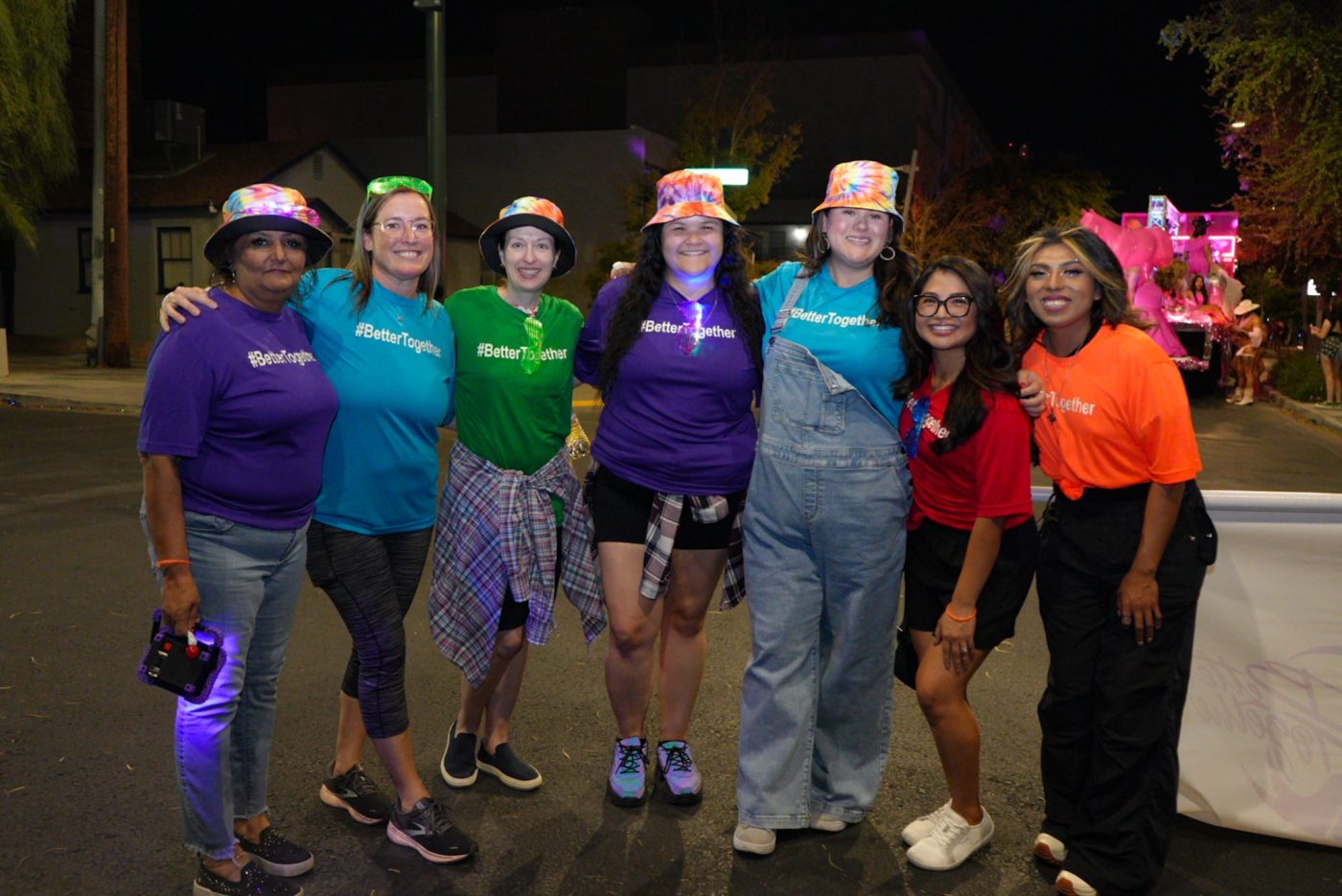 Seven individuals in purple, blue, green, red and orange t-shirts pose for a photo.