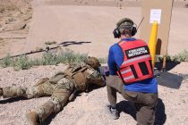 A firearms instructor wearing a red vest kneels next to a member of the NNSS Protective Force.