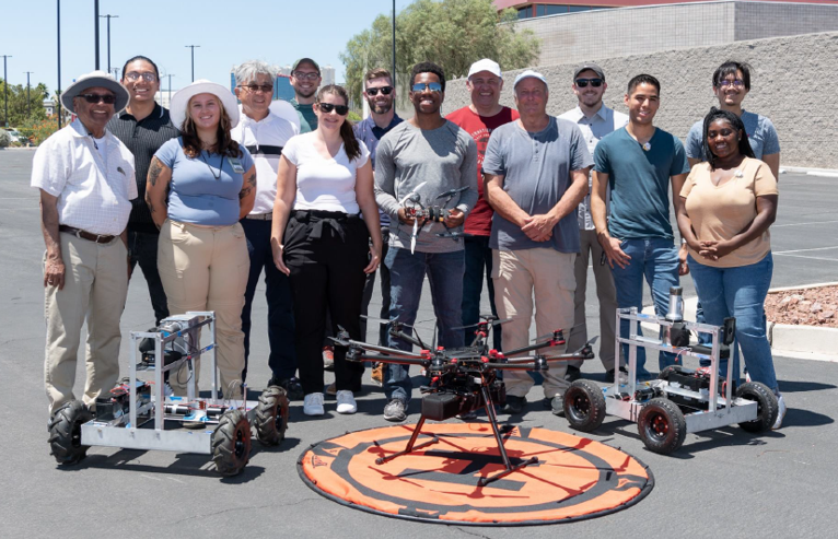 A group of students and mentors stand with Unmanned Aircraft Systems.