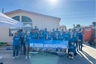 NNSS employees stand in front of a house with a sign that reads "We secure America's future."