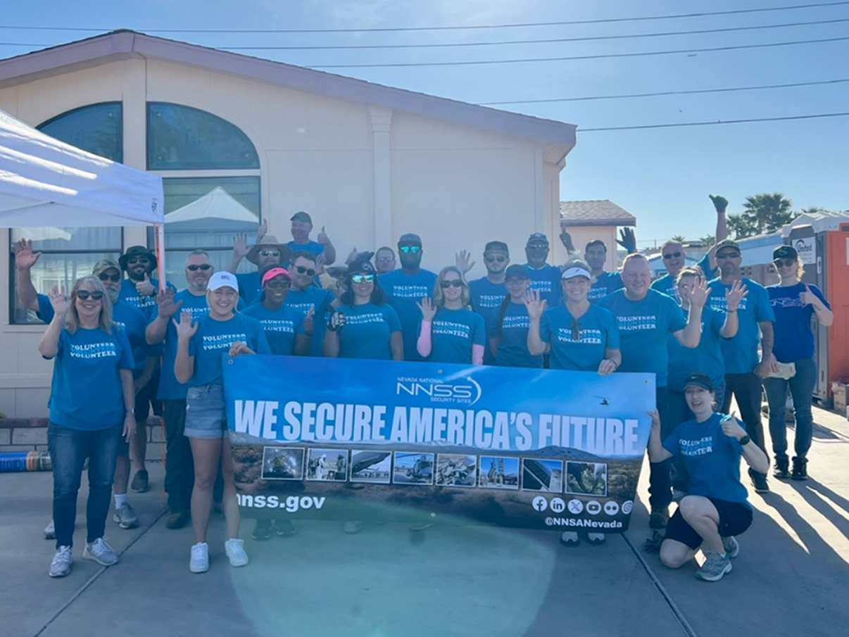 NNSS employees stand in front of a house with a sign that reads "We secure America's future."