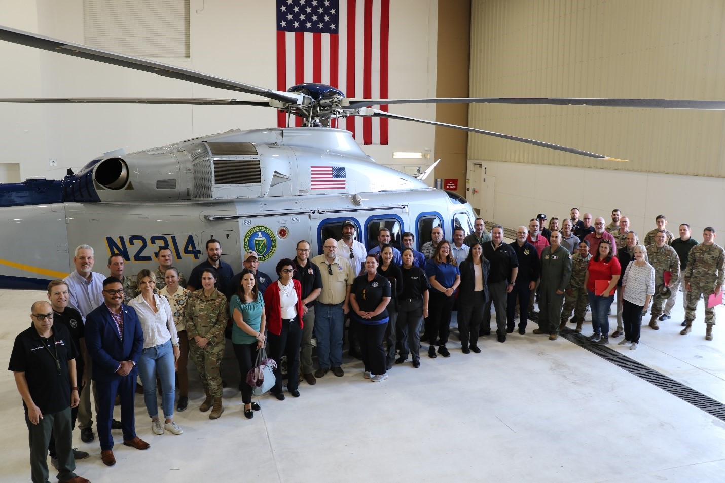 A group stands in front of a helicopter inside an aviation hangar.