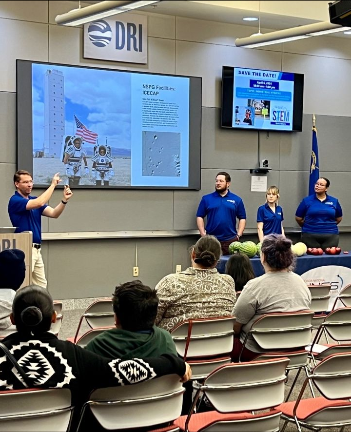 NNSS scientists in blue shirts speak about NASA astronauts training at the Site to an audience.