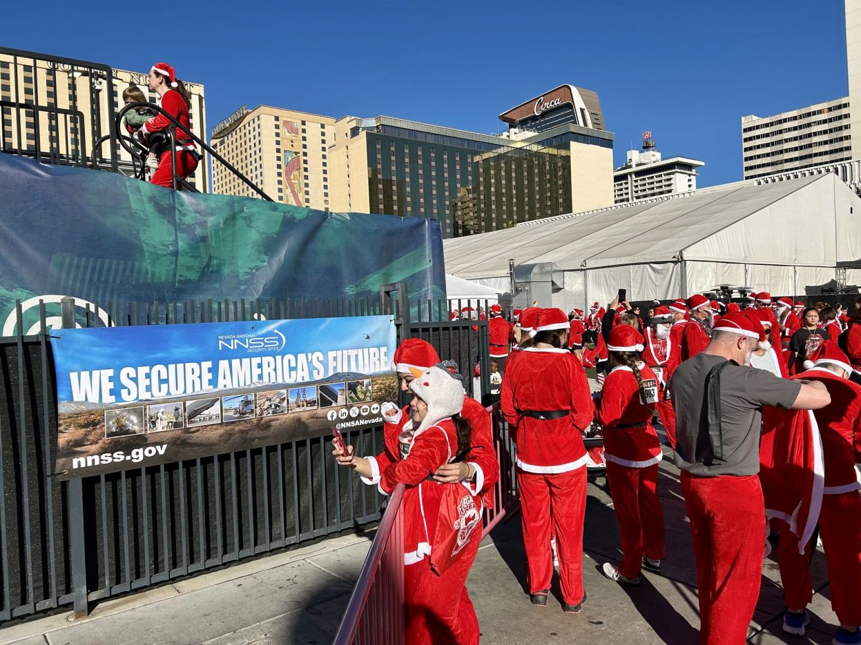 Individuals in red suits stand next to a banner that reads, "We secure America's future."