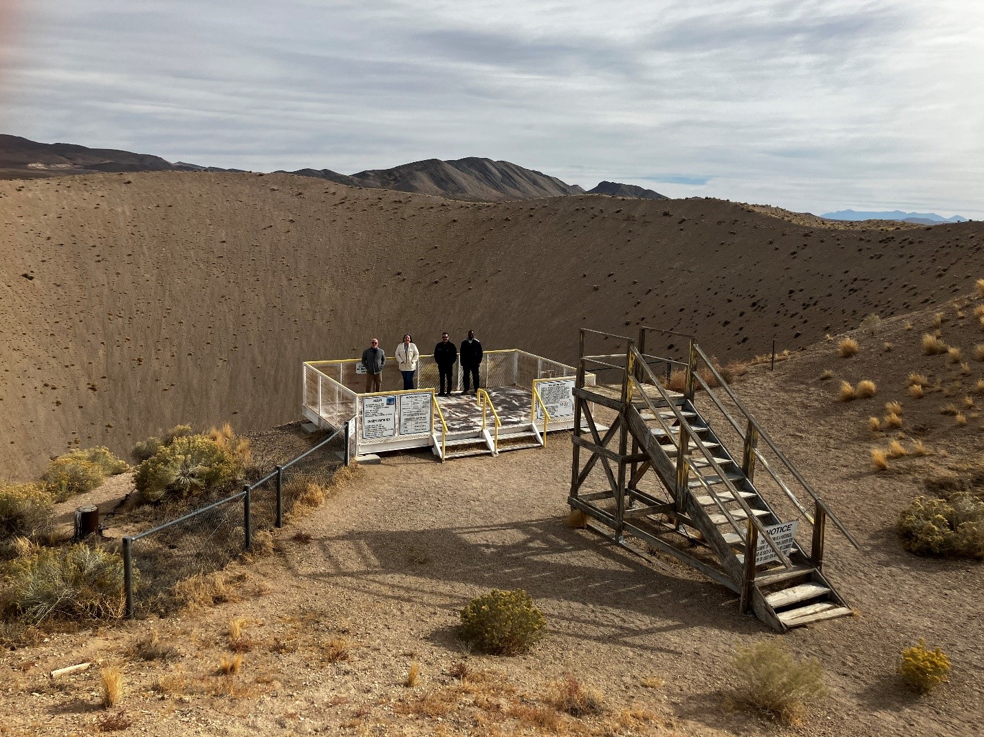 four people stand on platform in front of large crater